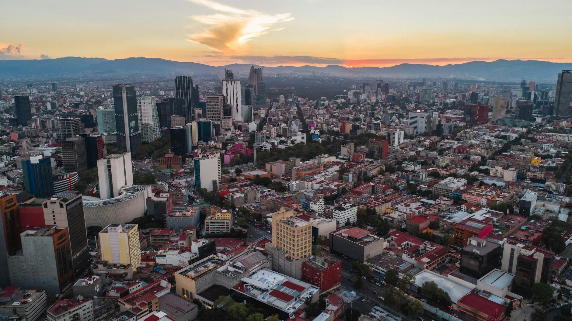 Atmospheric warm-toned aerial view of Latin American city skyline at golden hour, deep teal and amber color grade, soft focus on modern office towers with mountains in background, editorial architectural photography