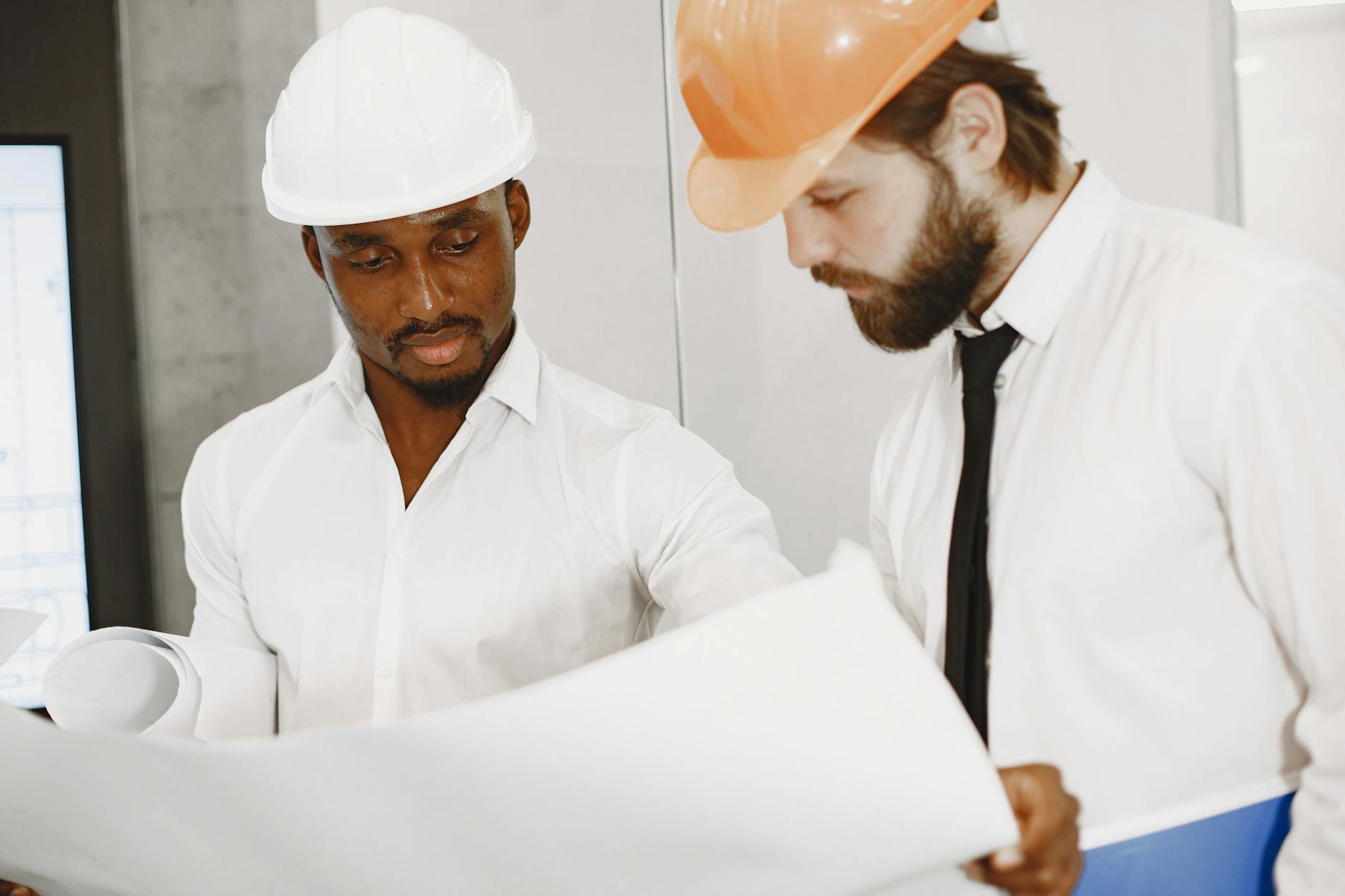 Project coordinator reviewing construction blueprints with hard hat on desk